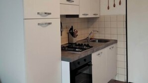Pieni, käytännöllinen keittiö, jossa on valkoiset kaapit, kaasuliesi, uuni ja pesuallas.