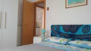 Makuuhuoneessa on sänky, yöpöytä, lamppu, ovi ja seinä, jossa on kehystetty taulu.