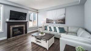 A modern living room with a fireplace, a flat-screen TV, a sofa, and a coffee table. - Entire Executive Home, Walk to lake! (Chestermere)