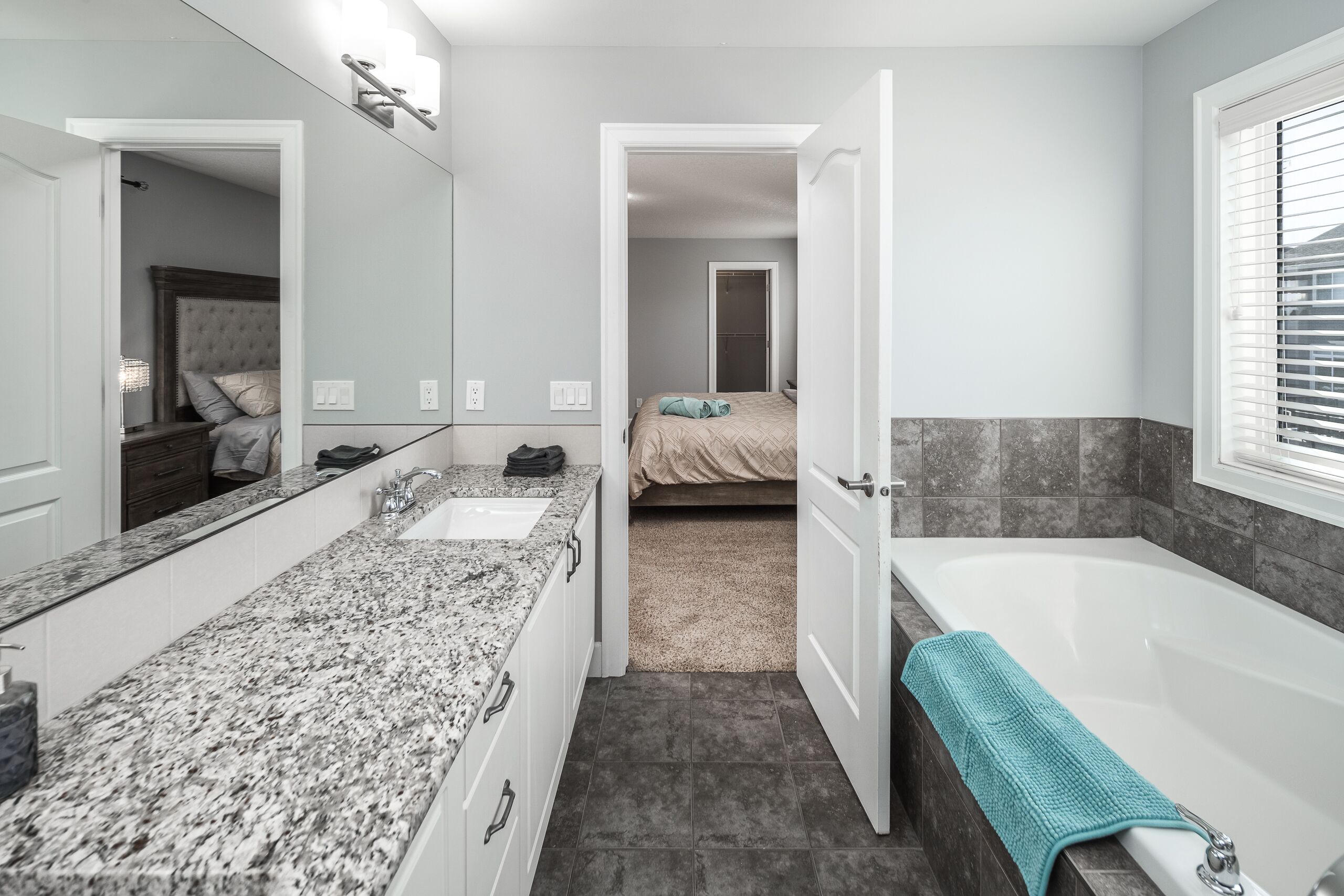 Ein modernes Badezimmer mit einer Granit-Arbeitsplatte, einer weißen Badewanne und einer sichtbaren Tür zu einem Schlafzimmer.