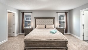 A bedroom with a large bed, two bedside tables, a window with blinds, and a door. - Entire Executive Home, Walk to lake! (Chestermere)