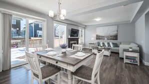 A spacious living area with a dining table, white chairs, and a fireplace. - Entire Executive Home, Walk to lake! (Chestermere)