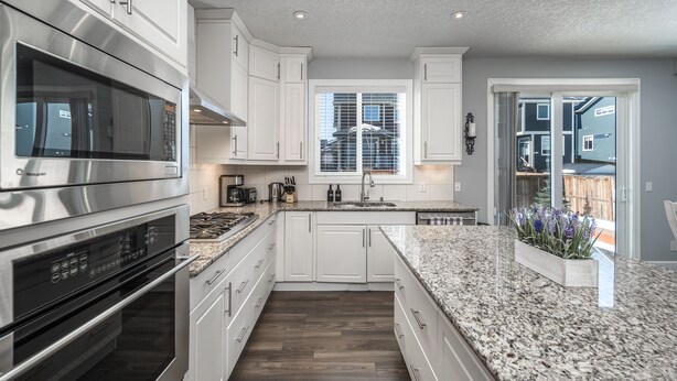 A modern kitchen with white cabinets, stainless steel appliances, granite countertops, and a window with blinds. - Entire Executive Home, Walk to lake! (Chestermere)