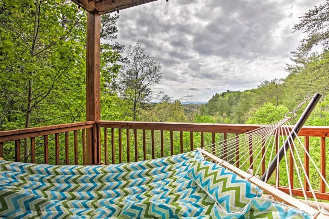 A hammock on a wooden deck with a patterned cushion, overlooking a forested landscape.