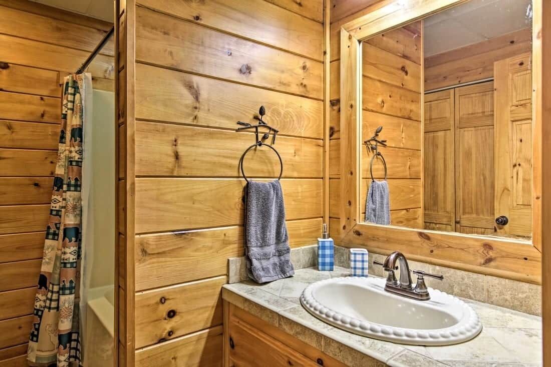 Une salle de bain rustique, avec des murs en bois, un grand miroir, un lavabo et des meubles de rangement en bois.