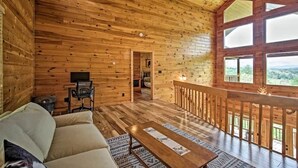 A wooden cabin interior with a sofa, a table, and a balcony with a railing.