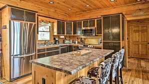 A cabin-style kitchen with wooden walls, a granite countertop, stainless steel appliances, and a bar area with animal print stools.