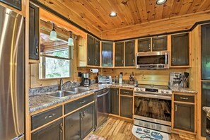 A modern kitchen with stainless steel appliances, wooden cabinets, and a granite countertop. - Blue Ridge Luxury Cabin w/ Views, Movie Theater, EV Charger & Hot Tub (Morganton)