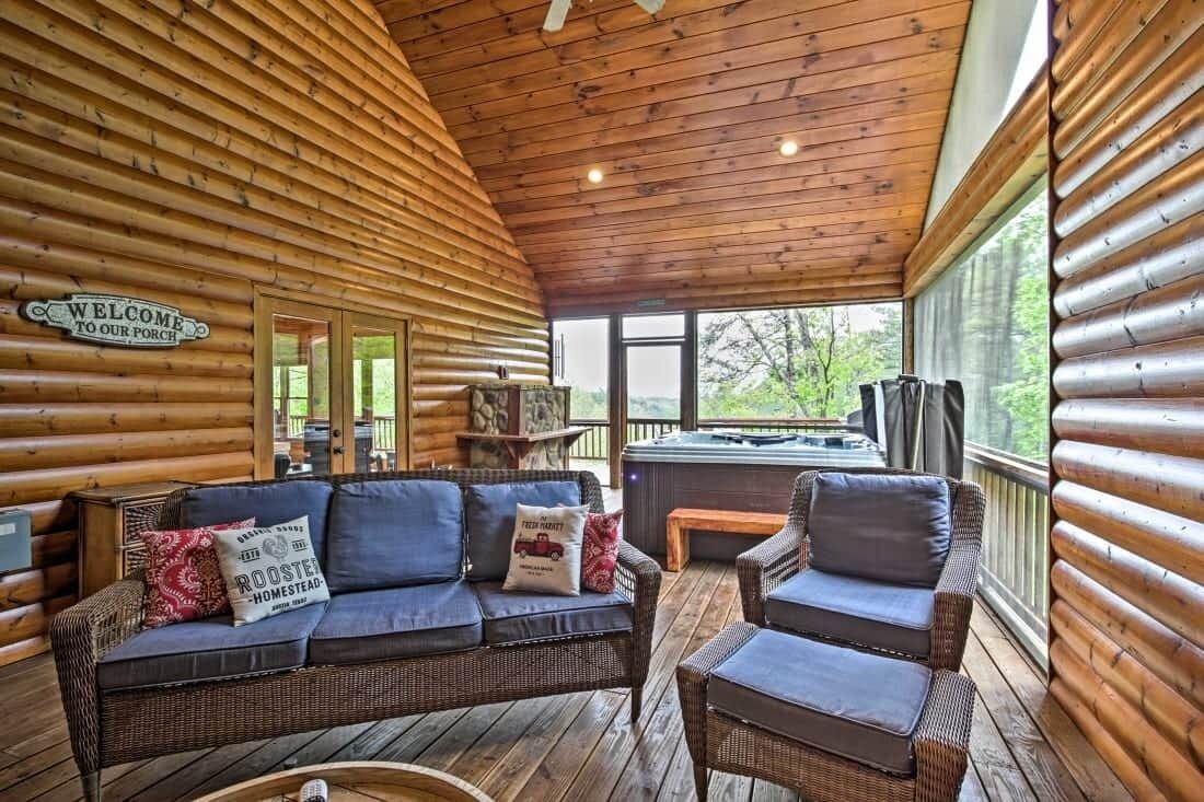 Interior de una cabaña de troncos con techo de madera, un sofá, una silla y un jacuzzi.