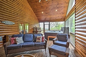 A log cabin interior with a wooden ceiling, a sofa, a chair, and a hot tub. - Blue Ridge Luxury Cabin w/ Views, Movie Theater, EV Charger & Hot Tub (Morganton)