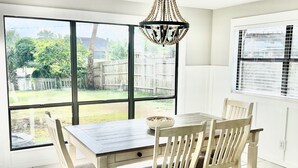 Un comedor con mesa y sillas, ventanas amplias y una araña.