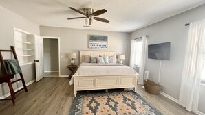 Un dormitorio con cama, ventilador de techo, televisor y alfombra.