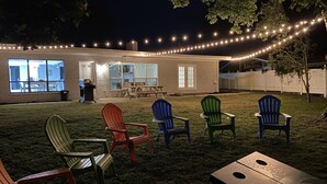 Un patio trasero con zona de estar, mobiliario exterior e iluminación con luces colgantes.