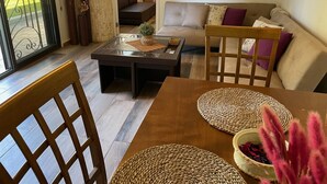 A living room with a glass-top coffee table, a sofa with cushions, and a dining table with chairs. - Chalet in Batroun, 1BR, gazon, 65sqm, parking, wifi (محافظة الشمال)