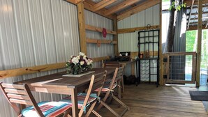 Un coin repas rustique, avec une table et des chaises en bois, un arrangement floral et une vue sur l’extérieur.
