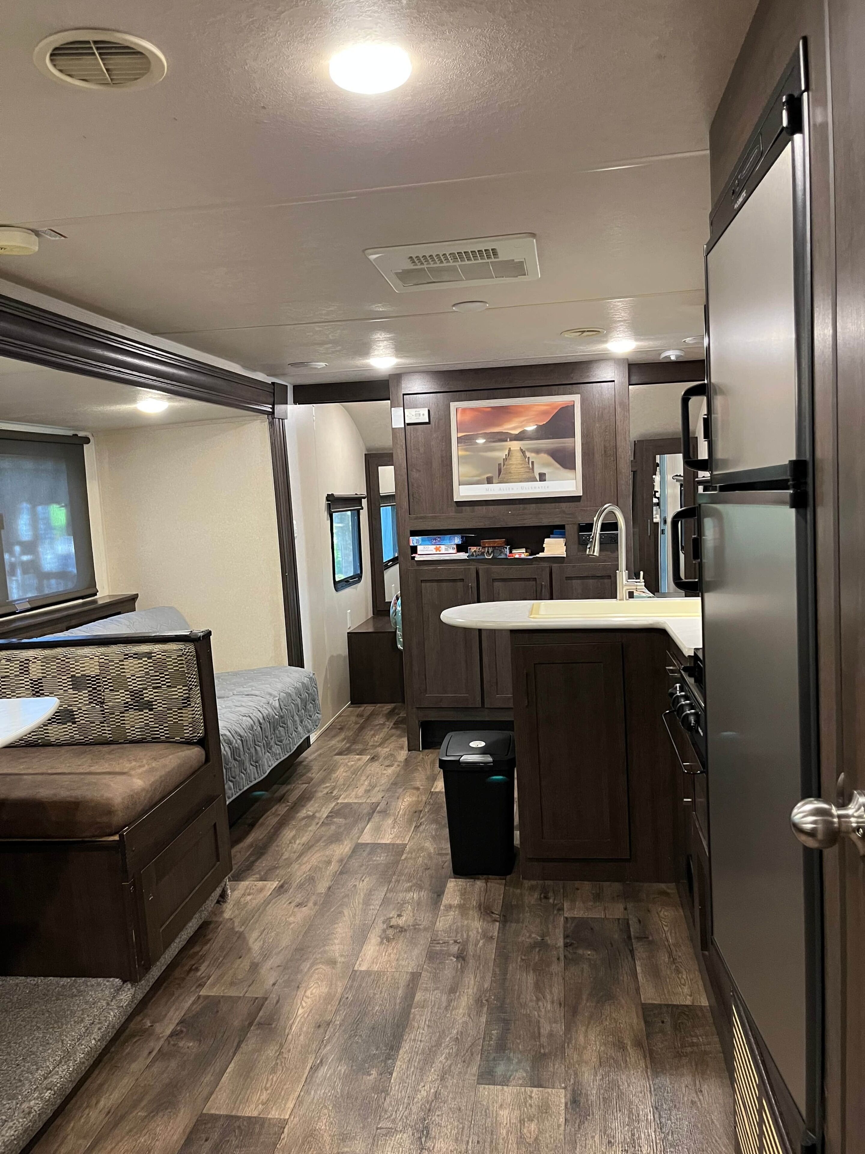 A compact RV interior with a kitchenette, a seating area with a sofa, and a small trash bin.
