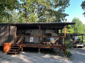 A rustic RV park with a covered RV, wooden steps, and a gravel ground. - Camper/ RV to Relax - camping (Hardin)