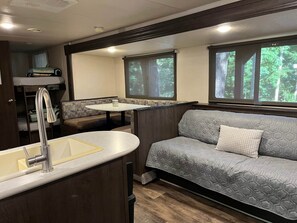A compact RV interior with a kitchenette, a seating area, and windows offering a view of the outdoors. - Camper/ RV to Relax - camping (Hardin)