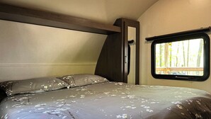 Un lit avec une couvre-lit à motifs floraux, une fenêtre donnant sur des arbres et une tête de lit en bois.