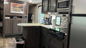 Une cuisine compacte avec des meubles en bois foncé, un réfrigérateur en acier inoxydable, un four à micro-ondes encastré, une cuisinière à gaz et un petit évier.