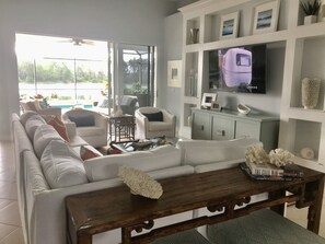 Relax in this spacious living room with a large sofa, coffee table, and TV, surrounded by decorative items and a beautiful view.