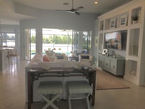 Relax in a spacious living area with a sofa, chairs, and dining table, offering a serene view of the pool and greenery.