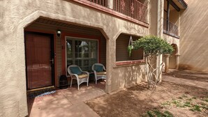 A two-story building with a red door, a covered porch with two wicker chairs, and a small tree. - Adorable Townhome (Midland)