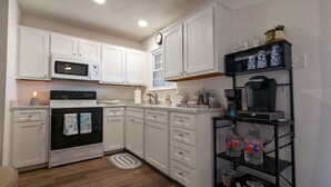 A kitchen with white cabinets, a microwave, an oven, a coffee maker, and a water dispenser. - Adorable Townhome (Midland)