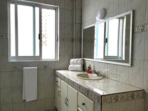 Un baño con un espejo grande, un lavamanos y una ventana.