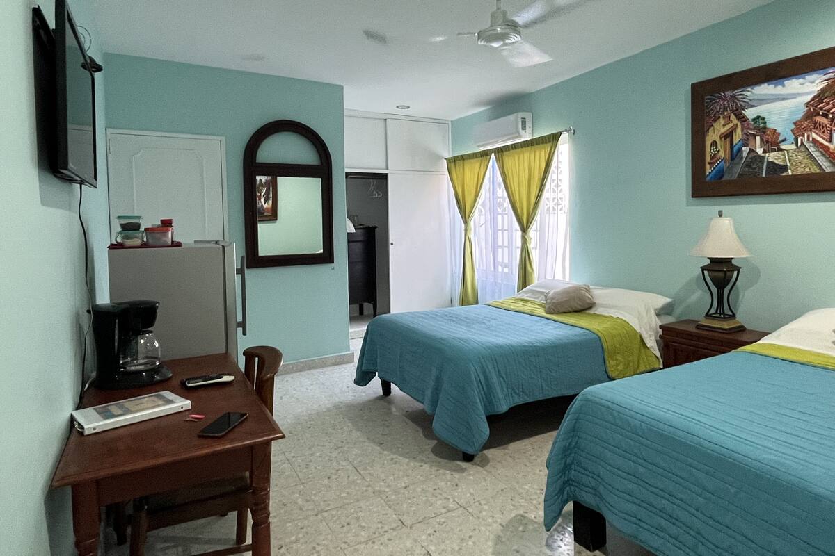 A hotel room with two beds, a desk with a coffee maker, a TV, and a ceiling fan.