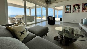 Un salón espacioso con un gran ventanal que da a un balcón con vistas al mar.