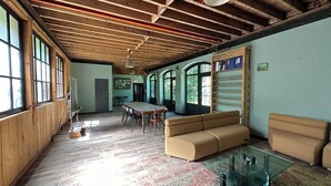 A spacious room with a high ceiling, wooden beams, a large dining table, and a sofa. - L'Orangerie du Château Loyd Pays de Caux (Les Hauts-de-Caux)