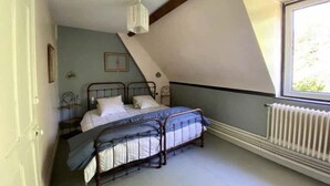 A bedroom with a sloped ceiling, a bed with a metal frame, a radiator, and a window. - L'Orangerie du Château Loyd Pays de Caux (Les Hauts-de-Caux)