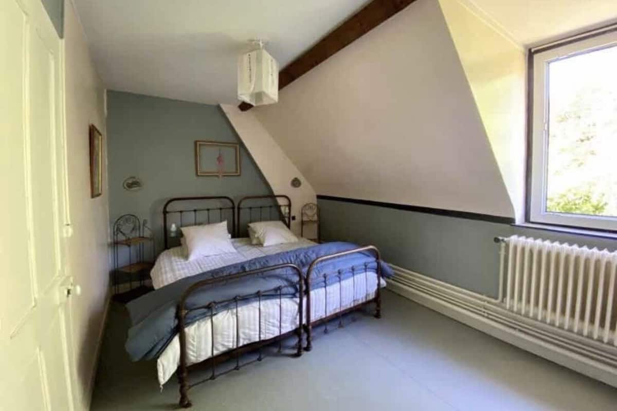 Ein Schlafzimmer mit schrägen Wänden, einem Bett mit Metallgestell, einem Heizkörper und einem Fenster.