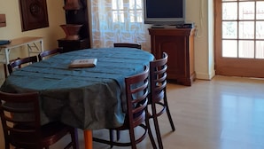 A dining area with a table set for four, a television on a stand, and a window with patterned curtains.