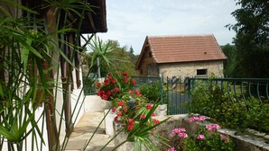 A stone-paved courtyard with potted plants and flowers, a stone building with a tiled roof, and a metal gate.