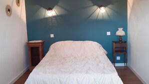 A bedroom with a large bed, two wall-mounted lights, a nightstand, and a small table with a lamp.