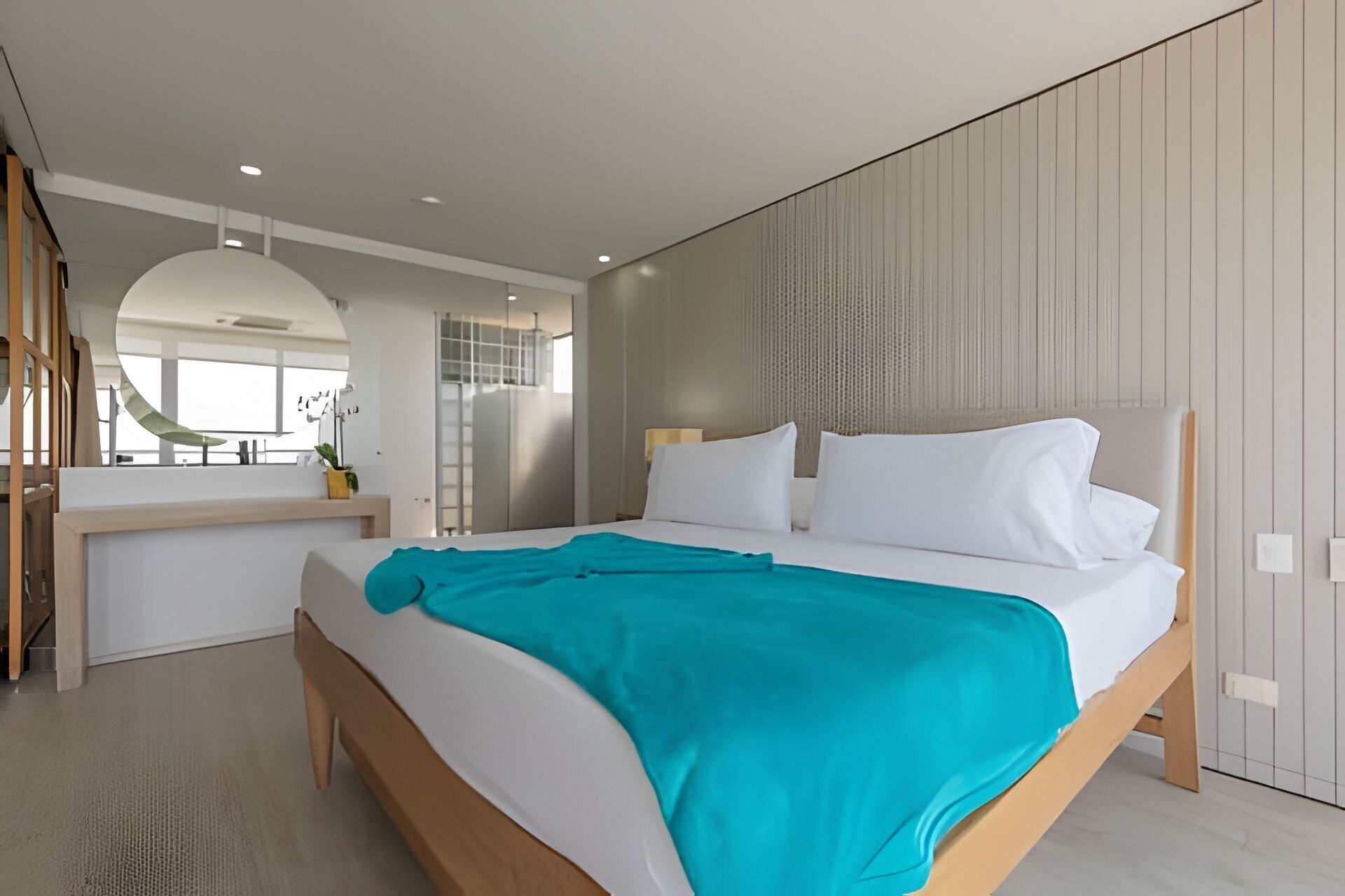 A modern bedroom with a large bed, a desk, and a view of the outdoors.
