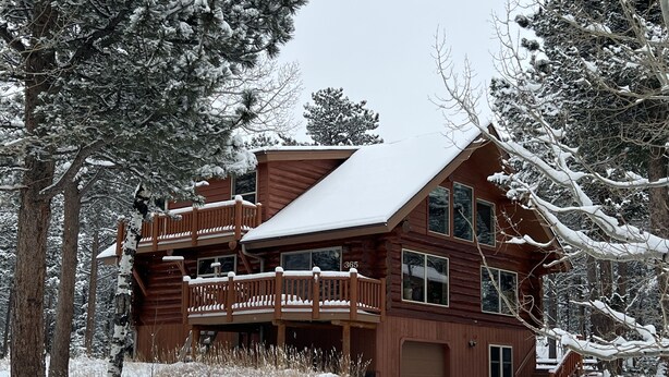 A multi-story log cabin with a snow-covered roof and deck, surrounded by trees. - Mountain Cabin Rentals (Ward)