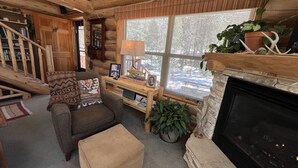 A cozy log cabin interior with a fireplace, a sofa, a coffee table, and a bookshelf. - Mountain Cabin Rentals (Ward)