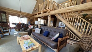 A cozy log cabin interior with a leather sofa, wooden coffee table, and a staircase leading to an upper level. - Mountain Cabin Rentals (Ward)