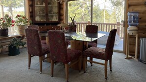 A wooden cabin interior with a dining table, chairs, a chandelier, and a water dispenser. - Mountain Cabin Rentals (Ward)