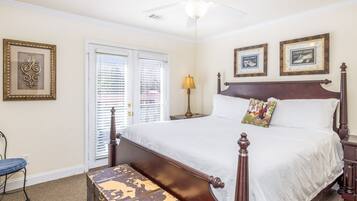 A bedroom with a four-poster bed, a wooden chest, a nightstand, a lamp, and two framed pictures on the wall.