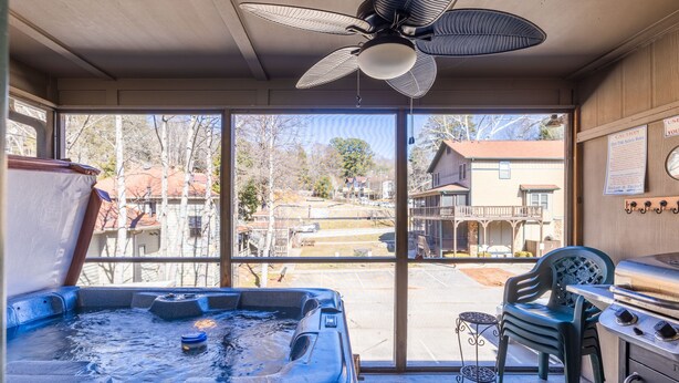 Uma banheira de hidromassagem com ventilador de teto, churrasqueira e vista para uma área residencial através de grandes janelas.