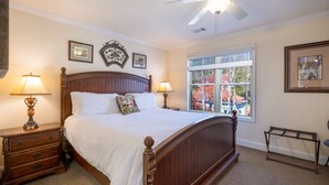 Quarto com cama de madeira, duas mesas de cabeceira com luminárias, ventoinha no teto e janela com vista para edifícios.