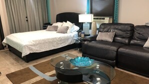 Un dormitorio con una cama, un sofá de cuero negro, una mesa de centro de vidrio y una mesita de noche con lámpara.