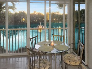 A dining area with a table and chairs, overlooking a body of water with a fountain. - Resort living-6 pools, tennis, boche and more! Lakefront unit! (Bonita Springs)