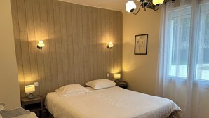 A bedroom with a wooden headboard, two bedside lamps, a bed with white bedding, a marble bedside table, and a window with sheer curtains.