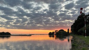 A calm river at sunset with a red and white flag on the right.