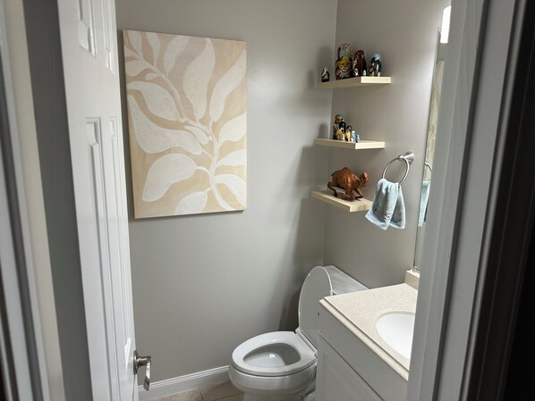A bathroom with a toilet, a sink, a towel rack, and a shelf with decorative items. - House for Graduation Weekend in Blacksburg, VA 5 minutes from campus! (Blacksburg)